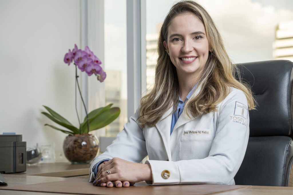 Dra Viviane, neurologista, sentada na mesa em seu consultório