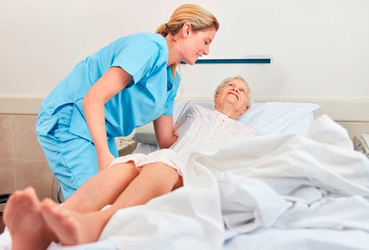 Idoso acamado, sendo ajudado por enfermeira