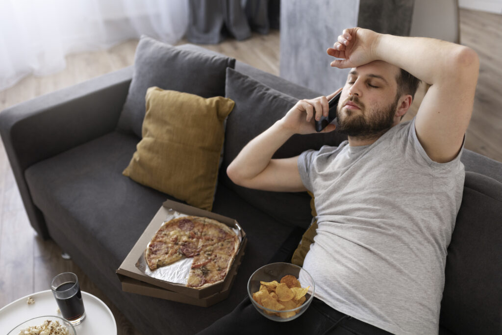 Homem sedentário no sofá, comendo alimentos ruins para o organismo